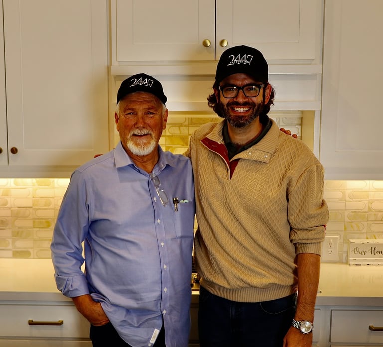 Two men wearing matching black caps with 24/47 logo standing together in a kitchen