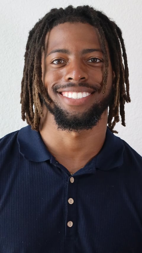 Smiling man with dreadlocks wearing a dark navy button-up shirt against a white background