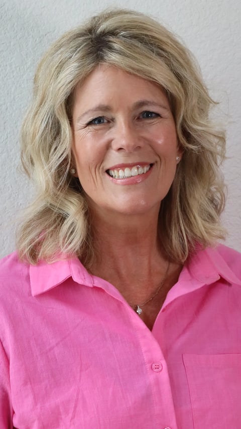 Portrait of a smiling woman with shoulder-length blonde wavy hair wearing a bright pink button-up shirt against a white background