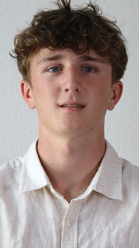 Portrait of a young man with curly brown hair wearing a white collared shirt against a light background