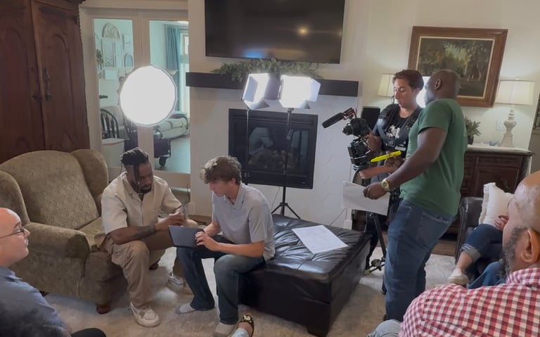 Video production crew filming an interview scene in a living room with professional lighting and camera equipment.