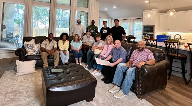 Large family gathering in a modern living room with people of various ages seated on brown leather furniture and standing in the background